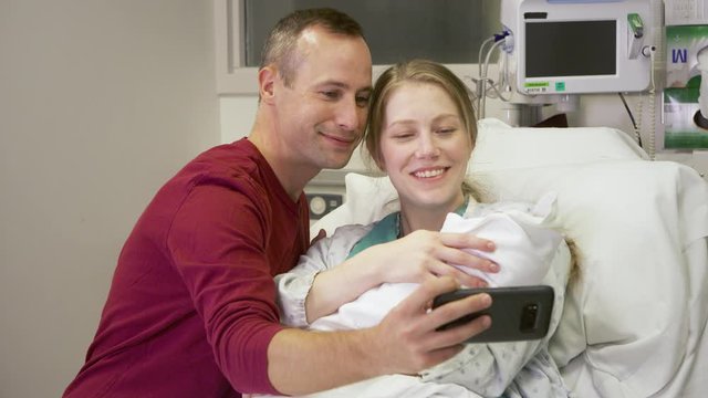 New parents take a selfie with their newborn baby for social media while at the hospital.