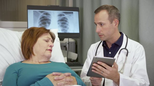 A sad patient holds back tears as she reacts to a bad prognosis from the doctor and he tries to console her while in hospital.