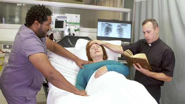A priest performing an exorcism on a woman in a hospital bed as a nurse helps hold her down.