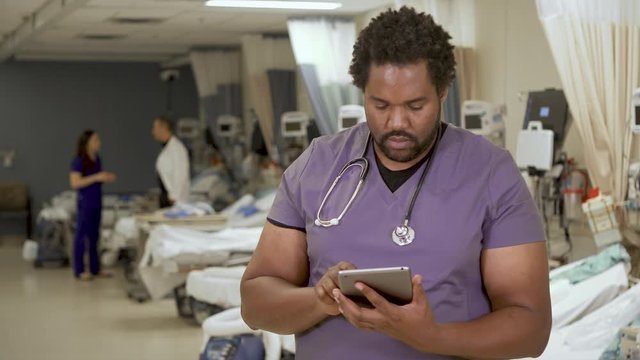 A black male nurse using a tablet computer in a modern hospital.
