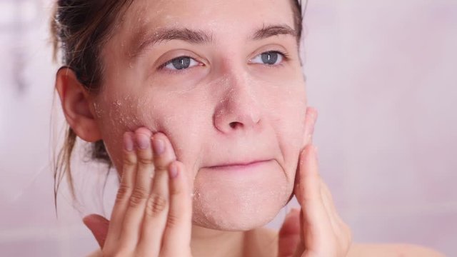 Skincare woman washing scrubbing face with facewash scrub. Close up  female young adult face cleaning skin.