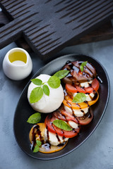 Black plate with caprese salad over grey concrete background, high angle view, studio shot