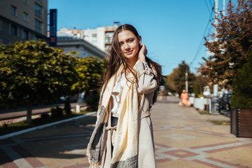 European woman in a cloak with long hair, straightens them by the ear on the street of a European city