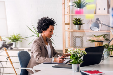 Happy smiling african-american business woman working on laptop at office. Businesswoman sitting at...