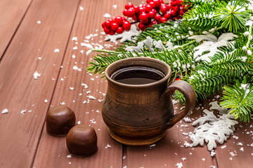 Christmas hot coffee background. New Year fir tree, dog rose, fresh leaves, chocolate candies and artificial snow. Wooden boards backdrop