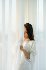 Young woman asian people in the bedroom with white curtains and the morning atmosphere when the sun shines.