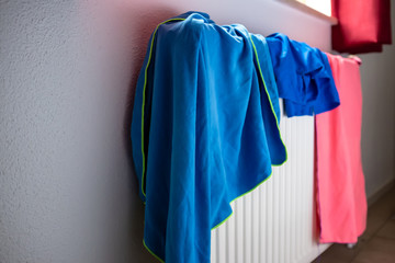 Bright towels and shorts are dried on a hot radiator after being used in the pool.