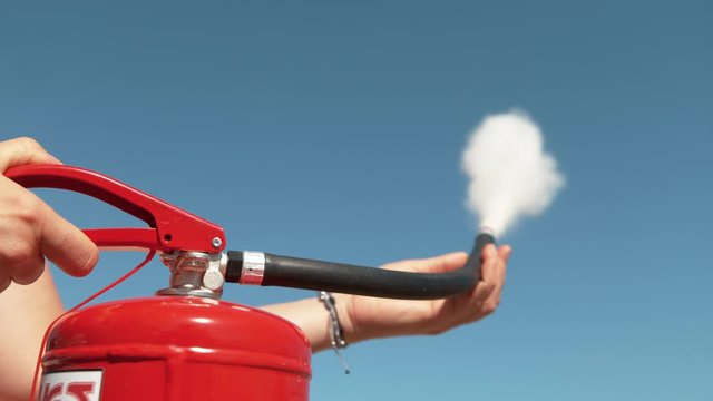 SLOW MOTION, CLOSE UP, DOF: Unrecognizable person squeeze the handle of a fire extinguisher, causing white smoke and foam to come out of the nozzle. Young woman uses a fire extinguisher outdoors.