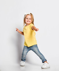 Cool dancing frolic kid baby girl in yellow t-shirt is playing having fun good time pointing at us feeling great