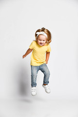 Active playful kid baby girl blonde in yellow t-shirt, blue jeans and sneakers is jumping high, having fun, flying