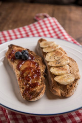 Fototapeta na wymiar Slices of rustic bread with peanut butter, banana, blueberries, cinnamon, maple syrup and strawberry jam. Vertical, copyspace.