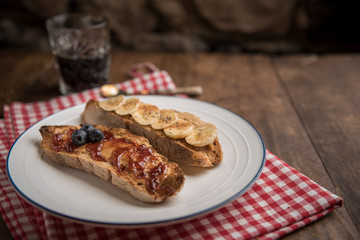 Bread slices on rustic table with peanut butter, banana, blueberries, cinnamon, maple syrup and strawberry jam. Black coffee in the background. Copyspace. Horizontal