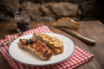 Healthy breakfast, sourdough country toast with peanut butter, banana, blueberries, cinnamon, maple syrup and strawberry jam. Bread and black coffee in the background. Horizontal