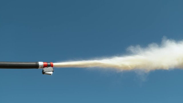 SLOW MOTION, CLOSE UP, DOF: Detailed shot of fire extinguisher nozzle emitting white powder. Small portable fire extinguisher is set off outdoors on a sunny day. White smoke comes out of a black hose.
