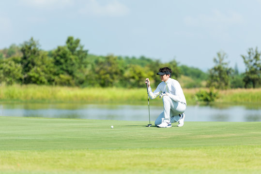 Professional Golfer asian man playing aiming shot for putting ball on the hole with club on green course.  Hobby in holiday and vacations in sunny morning day on club golf. Lifestyle and Sport Concept