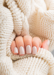 Stylish pastel beige Nails holding knitted wool material.