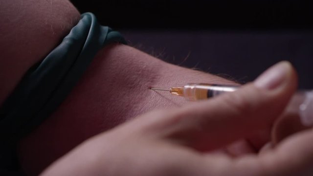 Close-up of a man putting a needle into his arm, with a strap tied around his bicep