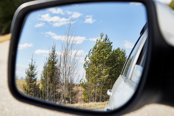 Side view mirror reflection of landscape with road and sky with clouds in sunny spring or autumn day