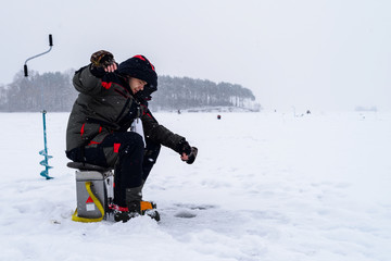Fototapeta na wymiar Winter fishing. Ice fisherman fishing on the lake in the cold winther day