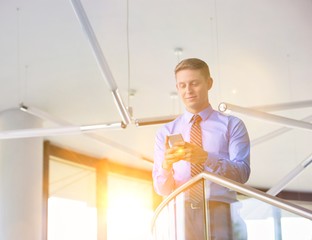 Smiling businessman using smartphone while standing at office