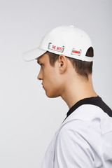 Cropped side photo of a dark-haired man, wearing white baseball cap with lettering 