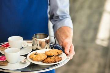 Young waiter serving coffee and cookies at restaurant