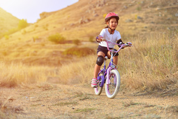 Fototapeta na wymiar Happy kid girl of 7 years having fun in autumn park with a bicycle on beautiful fall day. Active child wearing bike helmet