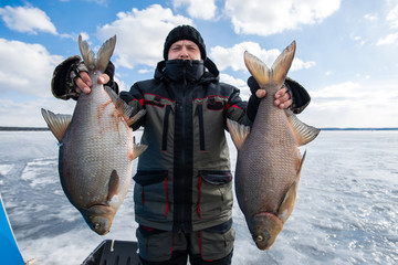 man and woman holding a pike on the ice. winter fishing
