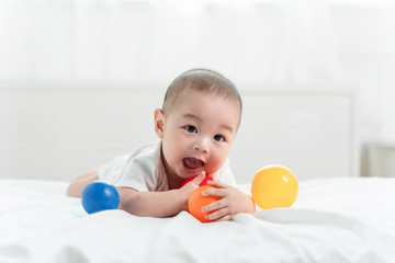 Asian baby is laughing and playing toy ball on white bed with feeling happy and cheerful and the baby that crawling on the bed.Baby family concept
