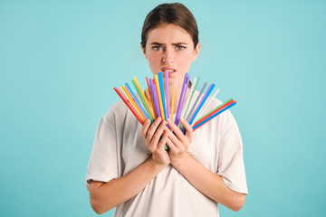 Confused girl holding colorful straws in hands disappointedly looking in camera over colorful background. Stop using plastic straws