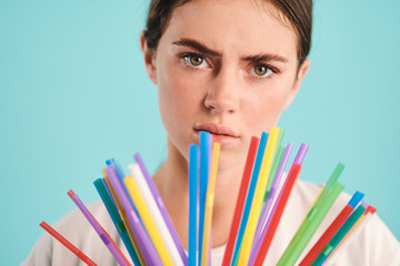Close up unhappy girl with plastic straws tiredly looking in camera over colorful background. Stop using plastic straws
