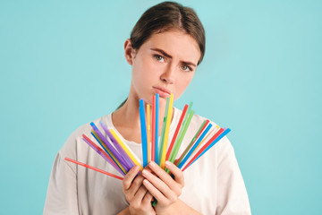 Upset girl holding plastic straws in hands sadly looking in camera over colorful background. Stop using plastic straws