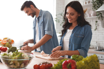 smiling wife and husband cooking dinner in the kitchen together - obrazy, fototapety, plakaty