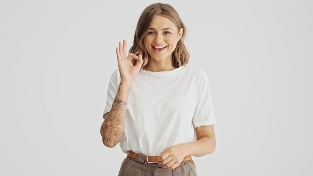 Smiling beautiful young woman wearing basic t-shirt showing ok gesture isolated over white background