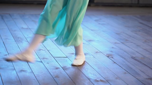 Close-up of a girl's legs in white ballet shoes on an old wooden floor during ballet training. Element of classical dance exercise.