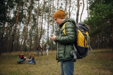 Group of friends on a camping or hiking trip in autumn day. Men and women with touristic backpacks going throught the forest, talking, laughting. Leisure activity, friendship, weekend.