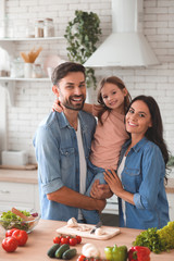 father holding daughter on the hands with mother standing near and smiling at the camera in the...