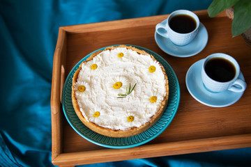 A cup of coffee and cream cheesecake stand on a wooden tray in bed.