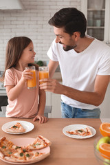 father clicking glasses with orange juice with daughter in the kitchen