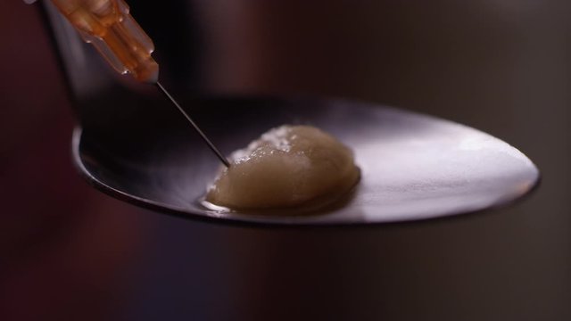 Extreme close-up of heroin getting sucked up into a needle through a cotton ball in a spoon