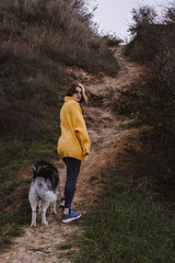 Naklejka na ściany i meble Young beautiful woman in yellow pullover sweater plays with a dog (grey and white husky) on the beach