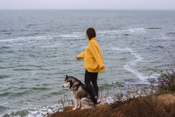 Young beautiful woman in yellow pullover sweater plays with a dog (grey and white husky) on the beach