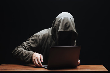 Criminal with laptop in hood on black background