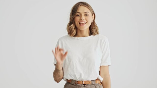Smiling young woman wearing a white basic t-shirt come in then show Ok gesture isolated over white background