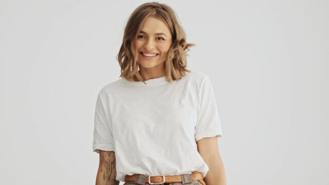 Charming young woman wearing basic t-shirt goes and turns around with beautiful smile isolated over white background