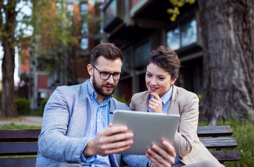 Business couple using digital tablet on park bench