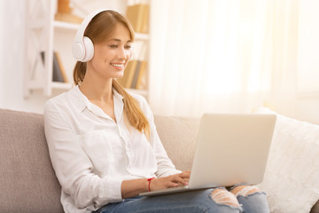 Woman In Headphones Using Laptop Sitting On Couch At Home