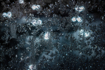 Dark frosty pattern on the window glass with blurred lights of night city. Abstract background