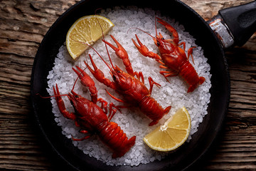 A pan with boiled crayfish stands on a textured brown wooden table top. View from above.