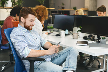 Confident guy texting on cellphone during team meeting